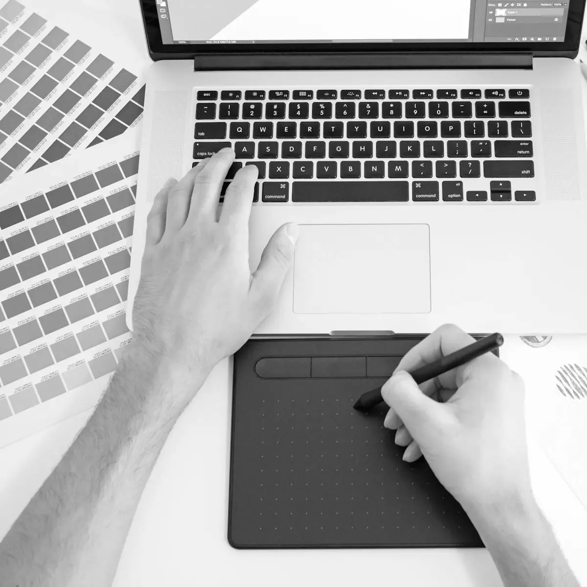 El diseñador trabaja en una computadora portátil con una tableta de dibujo, un abanico de colores y marcadores sobre la mesa